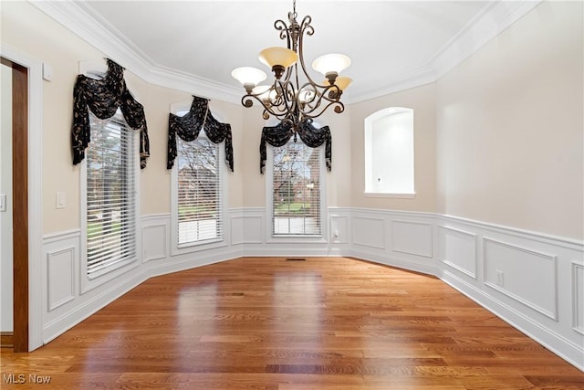 unfurnished dining area featuring ornamental molding, wood-type flooring, and a notable chandelier