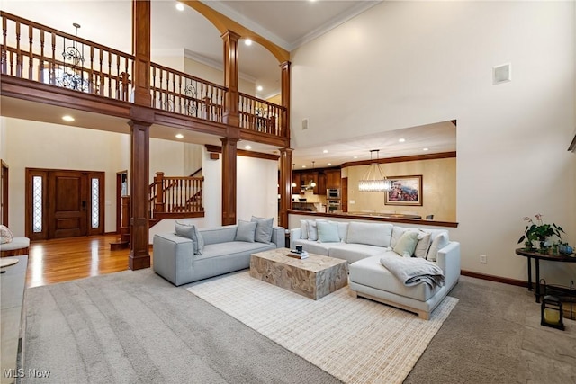 carpeted living room featuring crown molding, a towering ceiling, and ornate columns