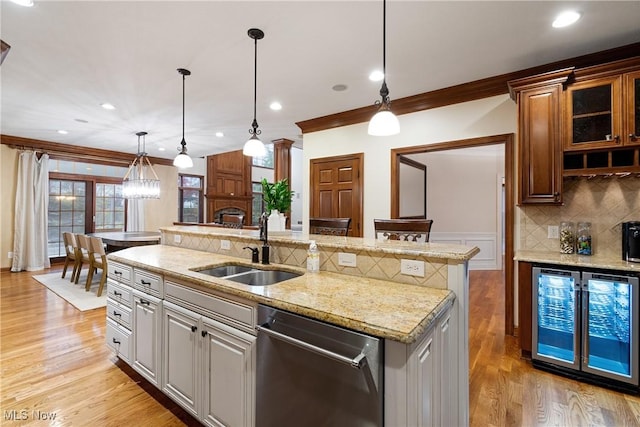 kitchen featuring sink, crown molding, stainless steel dishwasher, pendant lighting, and a kitchen island with sink