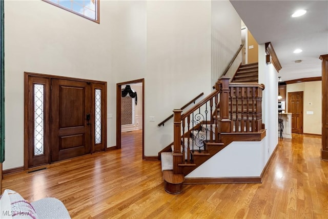 entrance foyer with crown molding, a towering ceiling, and light wood-type flooring