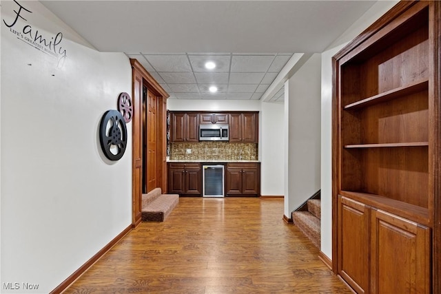 kitchen featuring wine cooler, light wood-type flooring, tasteful backsplash, and a drop ceiling