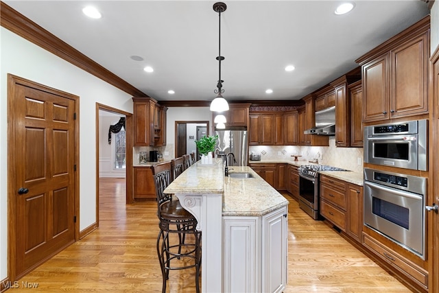 kitchen with sink, appliances with stainless steel finishes, a kitchen island with sink, light hardwood / wood-style floors, and decorative light fixtures