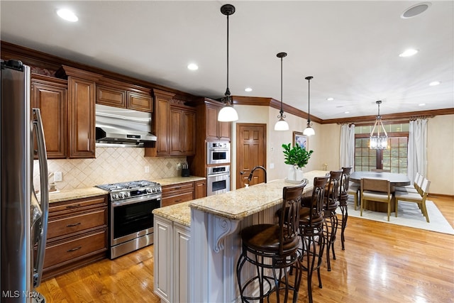 kitchen featuring a kitchen bar, light stone counters, hanging light fixtures, appliances with stainless steel finishes, and a kitchen island with sink