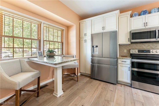 kitchen featuring appliances with stainless steel finishes, a breakfast bar area, decorative backsplash, light stone countertops, and light wood-type flooring