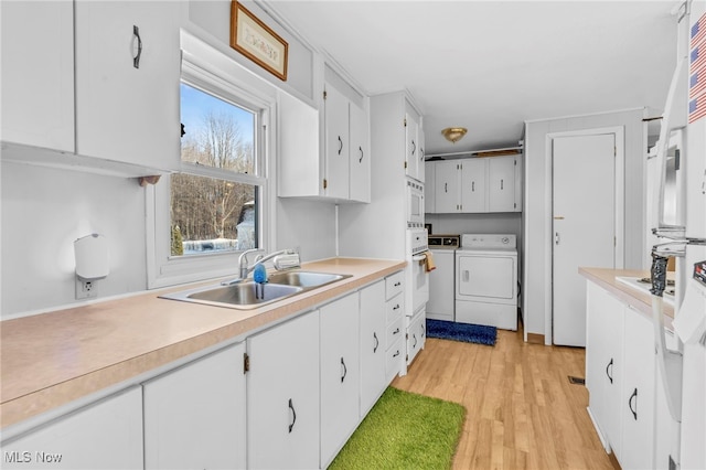 kitchen with washer and dryer, white cabinetry, sink, light hardwood / wood-style floors, and white appliances