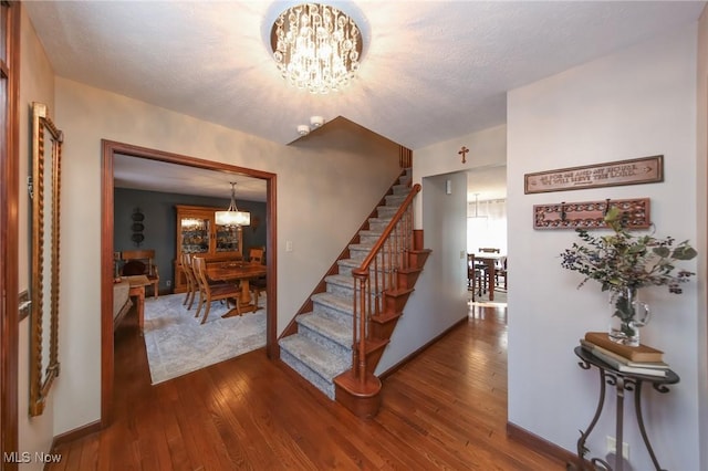 stairs featuring a textured ceiling, hardwood / wood-style flooring, baseboards, and a chandelier