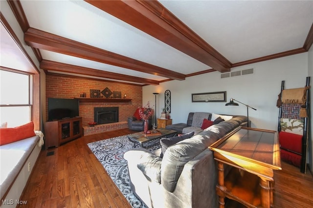 living room featuring beamed ceiling, ornamental molding, dark wood-type flooring, and a brick fireplace