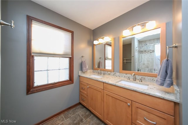 bathroom featuring a sink, baseboards, double vanity, and a tile shower