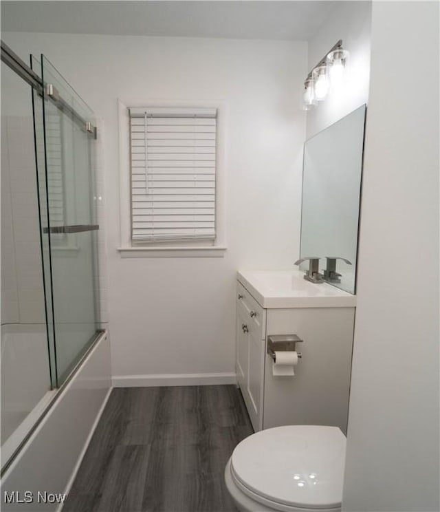 full bathroom featuring hardwood / wood-style flooring, vanity, combined bath / shower with glass door, and toilet