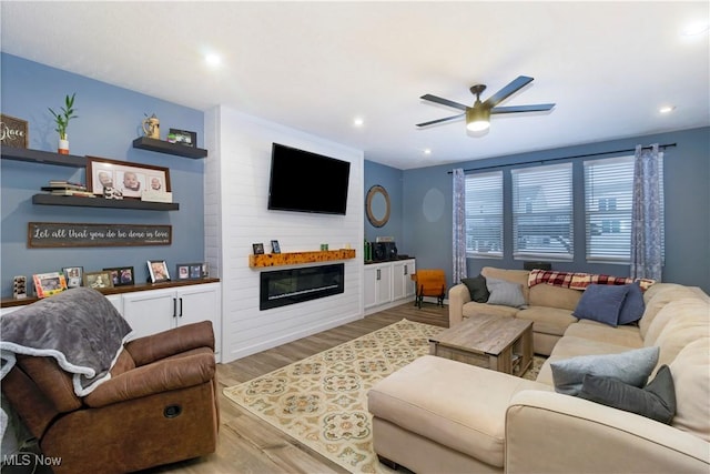 living room featuring ceiling fan, a large fireplace, and light hardwood / wood-style floors