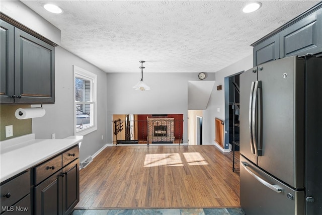 kitchen with stainless steel fridge, hardwood / wood-style floors, a fireplace, a textured ceiling, and decorative light fixtures