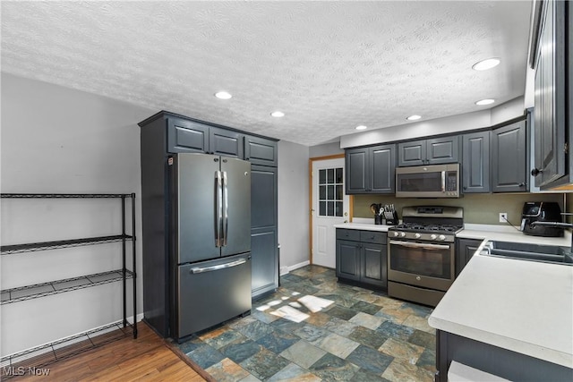 kitchen with stainless steel appliances, sink, a textured ceiling, and gray cabinetry