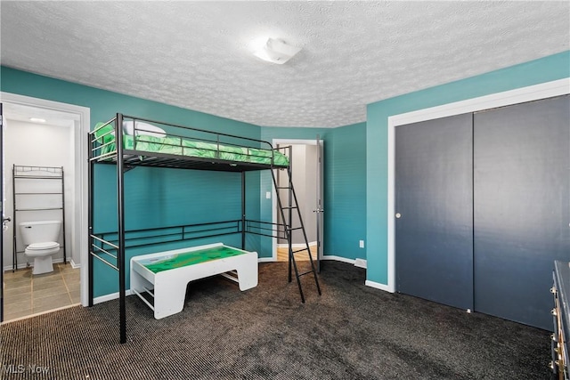 bedroom featuring ensuite bath, dark carpet, a closet, and a textured ceiling