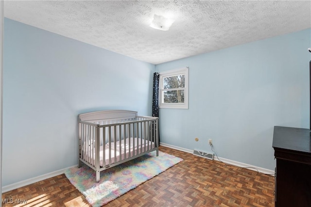 bedroom with dark parquet flooring, a crib, and a textured ceiling