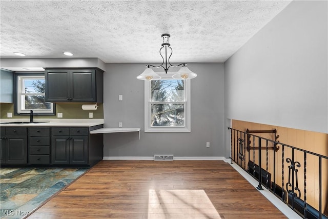 kitchen with sink, dark wood-type flooring, hanging light fixtures, and a textured ceiling