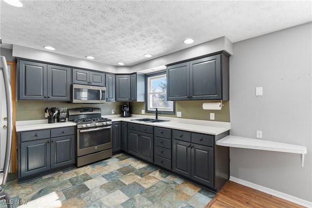 kitchen with appliances with stainless steel finishes, sink, a textured ceiling, and gray cabinetry