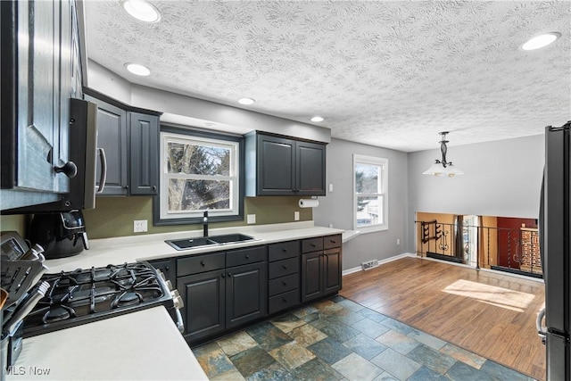 kitchen with sink, a textured ceiling, stainless steel refrigerator, pendant lighting, and black gas range