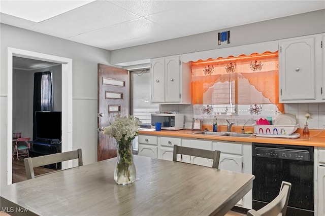 kitchen featuring white cabinetry, black dishwasher, sink, and tasteful backsplash