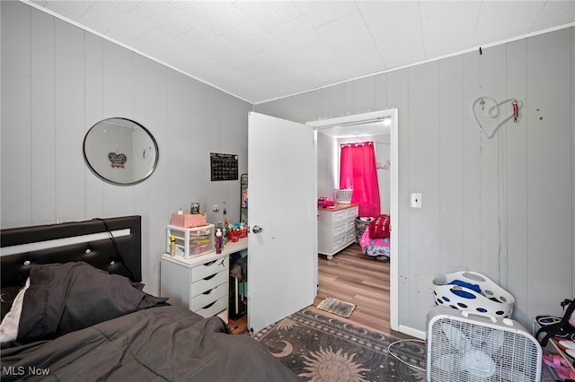 bedroom featuring hardwood / wood-style flooring, wooden walls, and crown molding