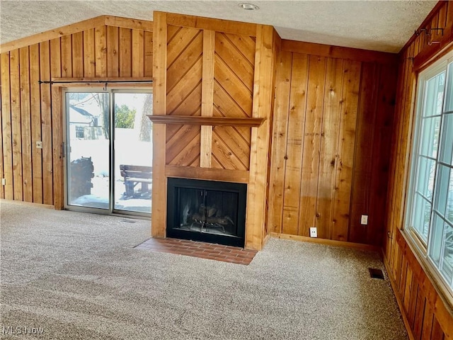 unfurnished living room with carpet, a textured ceiling, and wood walls