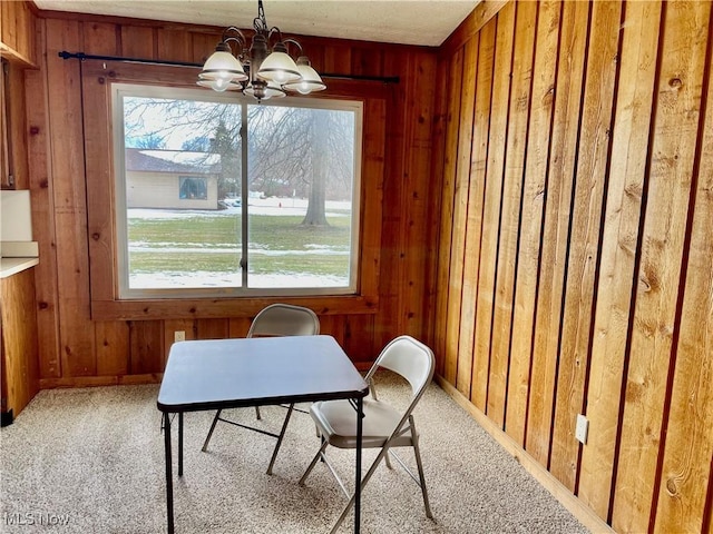 carpeted dining area featuring an inviting chandelier, a healthy amount of sunlight, and wood walls