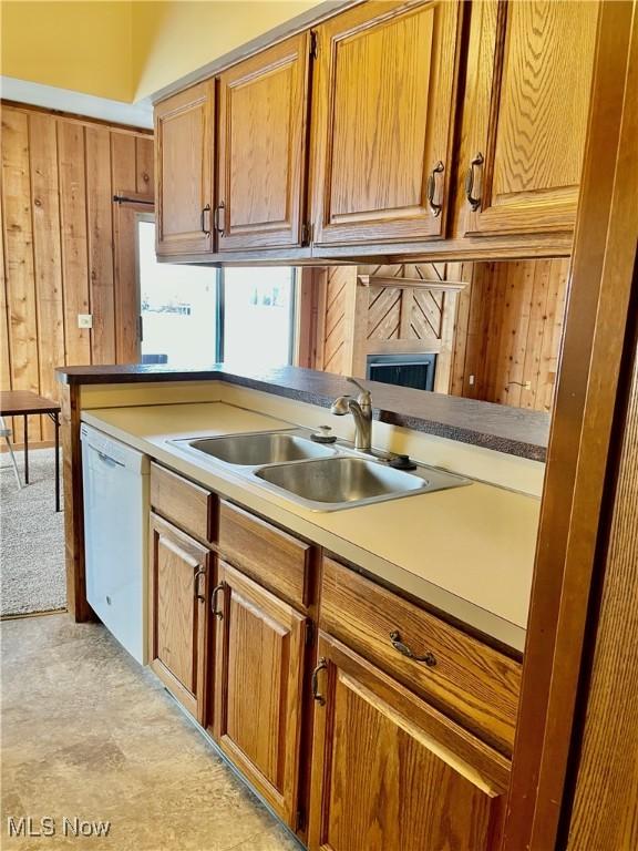 kitchen featuring white dishwasher, sink, and wood walls