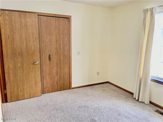 unfurnished bedroom featuring multiple windows, light carpet, and a closet