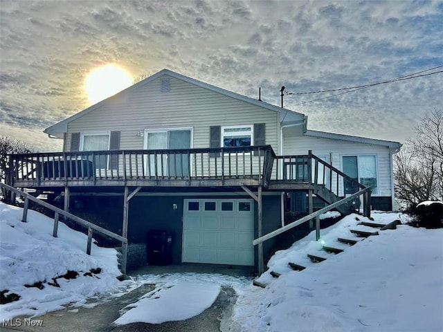 snow covered rear of property featuring a garage and a deck