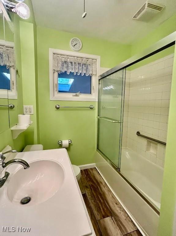 full bathroom featuring wood-type flooring, sink, shower / bath combination with glass door, and toilet