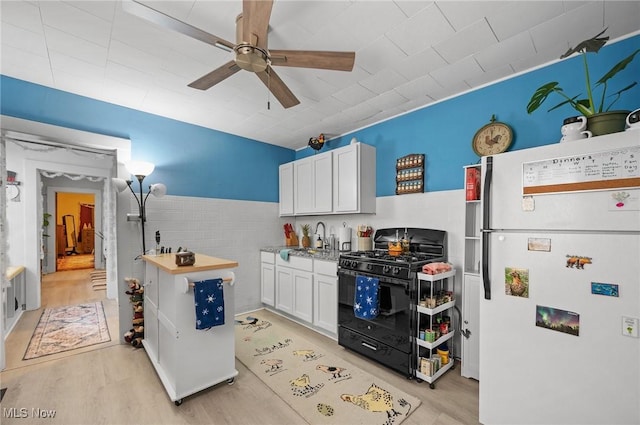 kitchen featuring white cabinetry, white fridge, black gas range oven, and tile walls