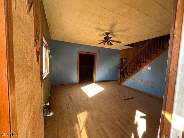 unfurnished living room with hardwood / wood-style floors, wooden walls, and ceiling fan