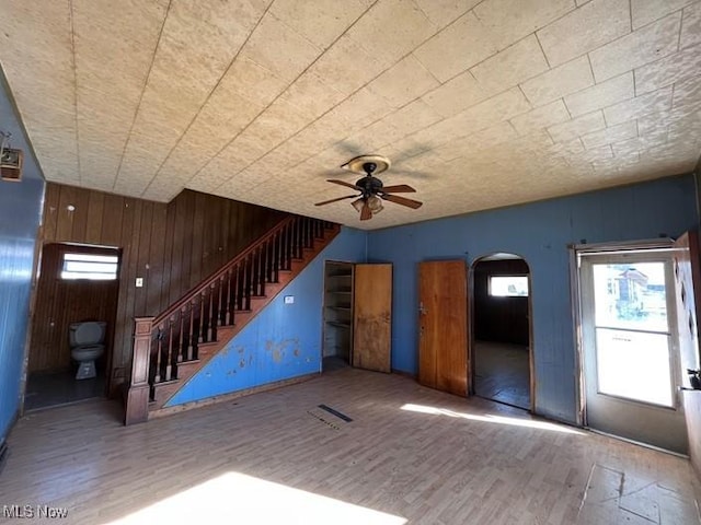 unfurnished living room with hardwood / wood-style floors, wooden walls, and ceiling fan