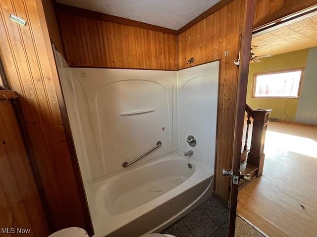 bathroom featuring shower / tub combination, ceiling fan, and wood walls