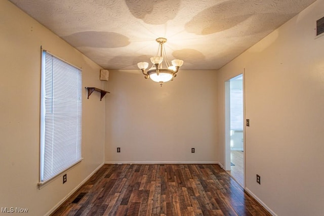 empty room with dark wood-type flooring, a textured ceiling, and a notable chandelier