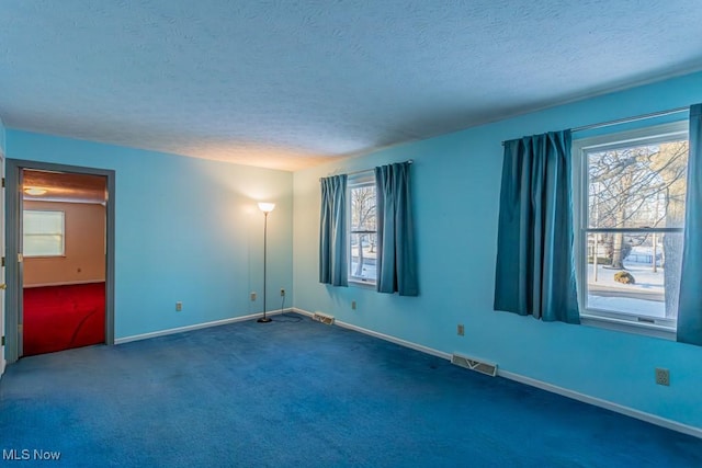 empty room with a wealth of natural light, a textured ceiling, and dark colored carpet