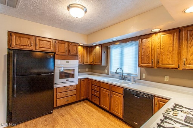 kitchen with light hardwood / wood-style floors, sink, a textured ceiling, and black appliances