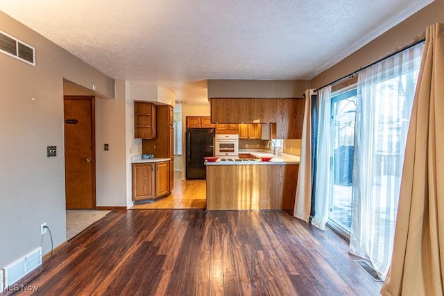 kitchen with white oven, kitchen peninsula, a textured ceiling, and black fridge