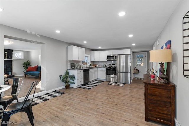 kitchen featuring appliances with stainless steel finishes, white cabinetry, a large fireplace, decorative backsplash, and light hardwood / wood-style flooring