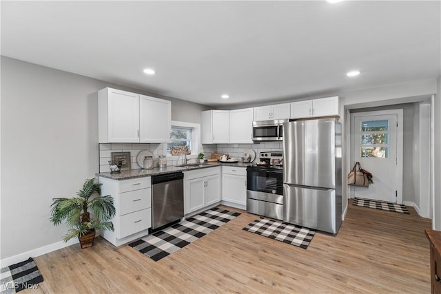 kitchen featuring white cabinetry, appliances with stainless steel finishes, light hardwood / wood-style flooring, and backsplash