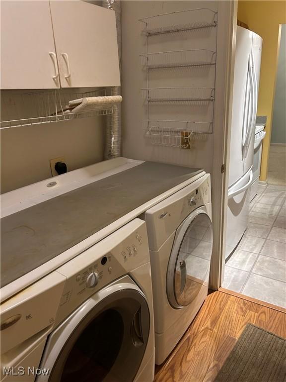 clothes washing area featuring cabinets, washing machine and clothes dryer, and light hardwood / wood-style flooring