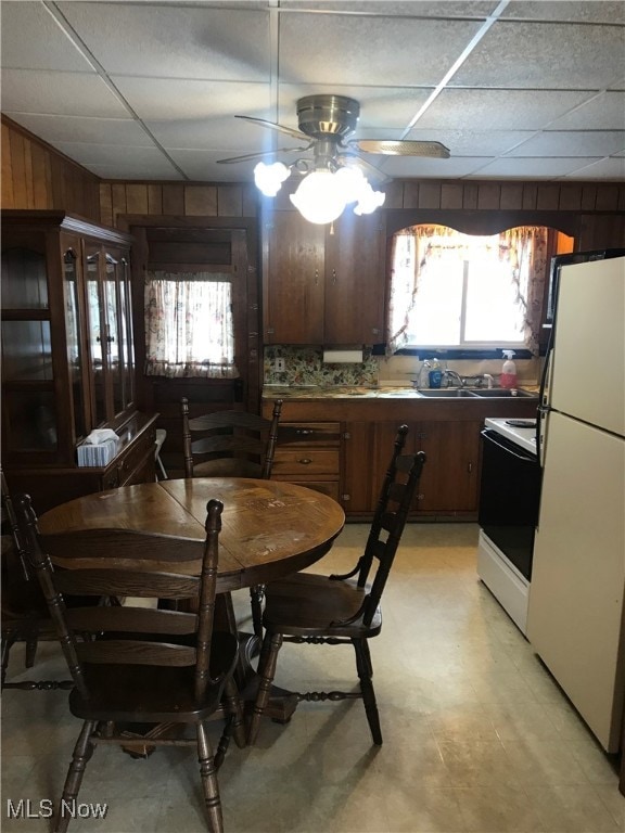 dining space with a paneled ceiling, wooden walls, and ceiling fan