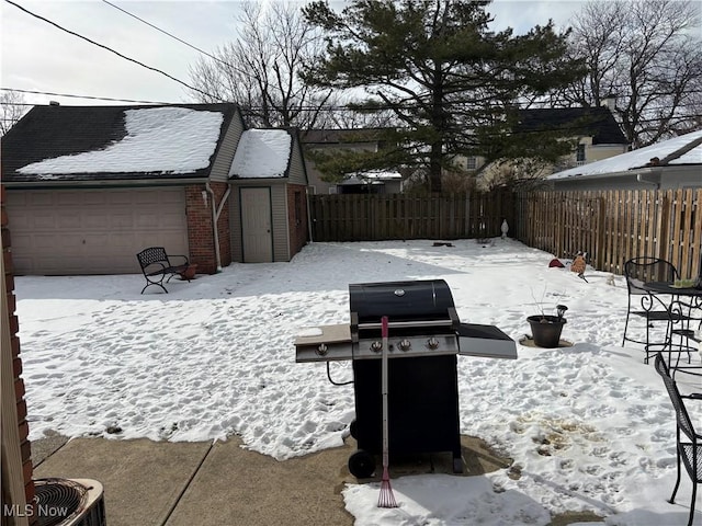 snow covered patio featuring a grill, an outbuilding, and a garage