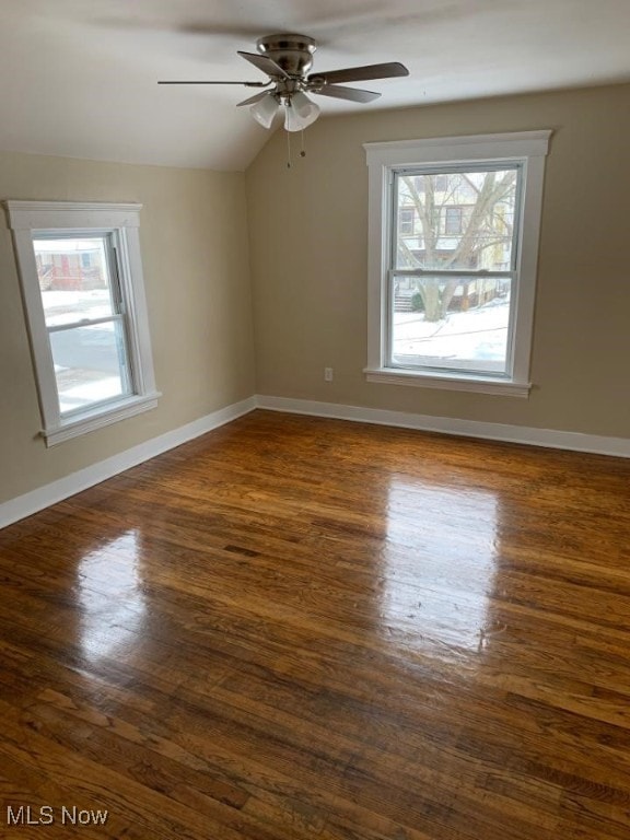 empty room featuring dark wood-style floors, vaulted ceiling, baseboards, and a ceiling fan