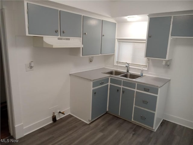 kitchen featuring under cabinet range hood, baseboards, dark wood-type flooring, and a sink