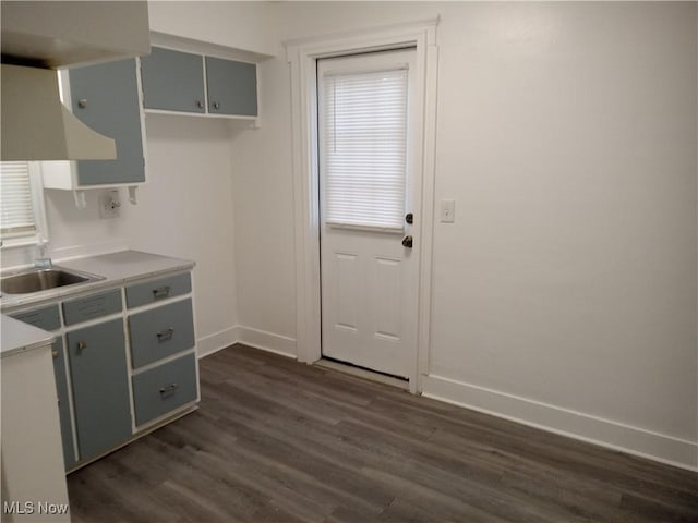 kitchen featuring light countertops, dark wood finished floors, a sink, and baseboards