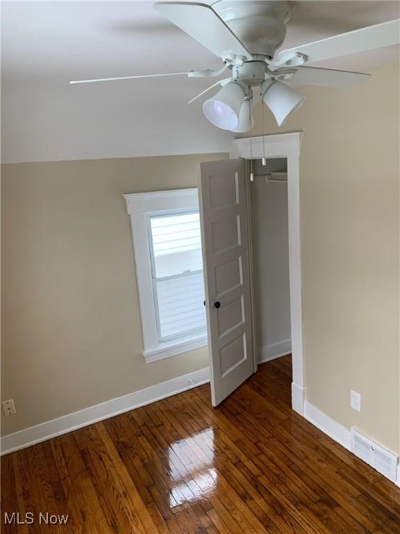 spare room featuring a ceiling fan, dark wood-style flooring, visible vents, and baseboards