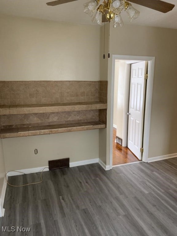 empty room with dark wood-style flooring, visible vents, ceiling fan, and baseboards