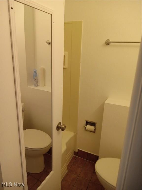 bathroom with tile patterned flooring, baseboards, toilet, and a bath