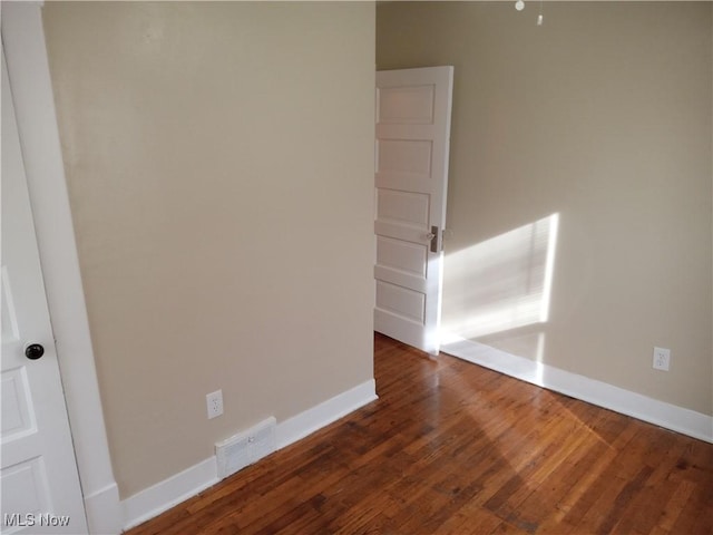 unfurnished room with dark wood-type flooring, visible vents, and baseboards