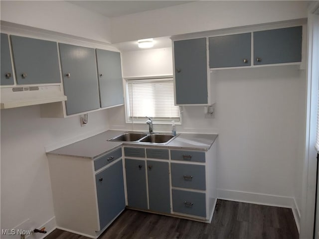 kitchen featuring under cabinet range hood, a sink, baseboards, gray cabinets, and dark wood finished floors